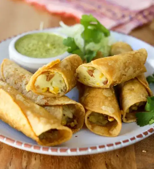 Potato taquitos on a plate with a green sauce and some garnish.