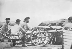 Three artillerymen crouch behind a small 2.5&nbsp;inch "Screw Gun" employed in the defence of Kimberley