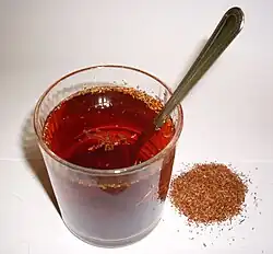 A cup of red tea with small bits floating in it